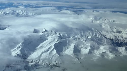 The Snowed Alps Mountains From the Sky, with the Majestic Peaks Emerging Through Fluffy Clouds
