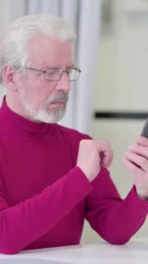 Senior Man Using Mobile Phone at Table Indoors