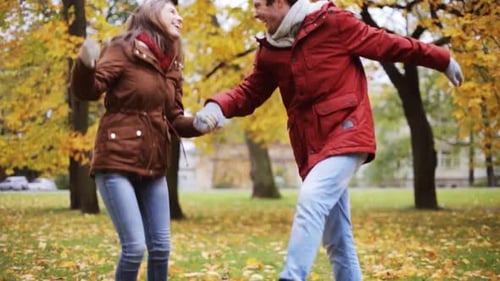 Happy young couple laughing and spinning in autumn park slow motion
