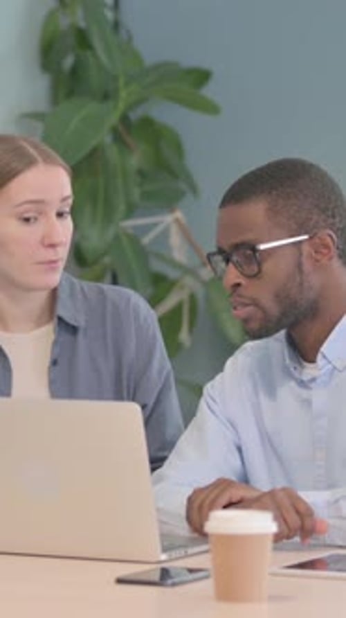 Colleagues Discussing Work at Desk with Laptop Indoors