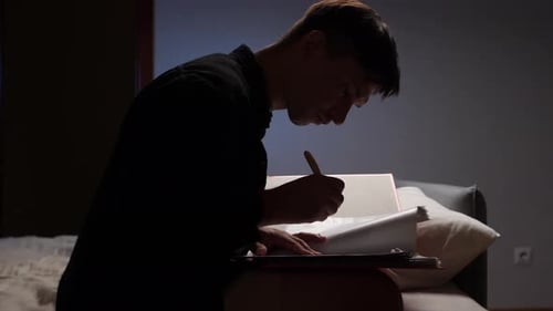 Focused Student Writing Notes at Night on Sofa in Bedroom