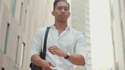 Young businessman looking at his wristwatch while standing in the business district