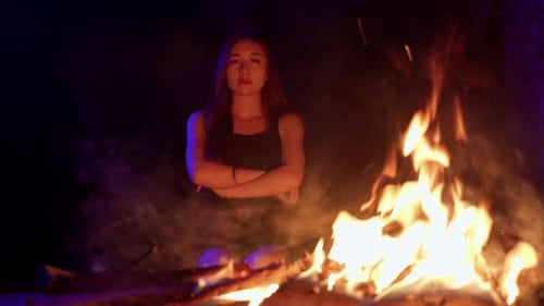 Woman Sits by Campfire in Dark Wilderness