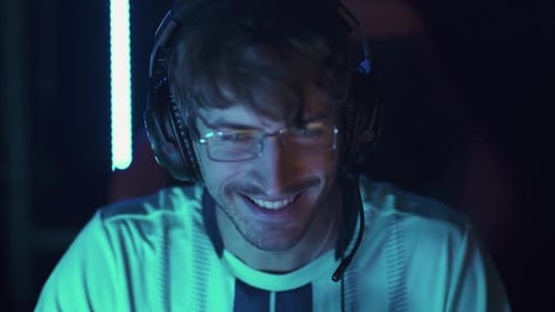 Excited Young Adult Gamer Wearing Headset in Dark Room