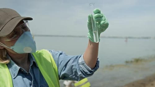Female Ecologist Checking Water Sample for Transparency on Beach