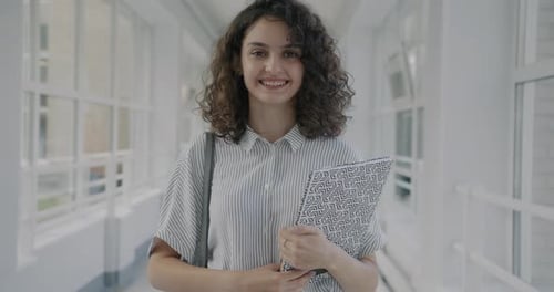 Portrait of Cheerful Girl Standing in Lobby of Modern University Holding Textbooks Smiling While