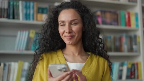 Happy Latina Hispanic Woman Student Using Mobile Phone Smartphone Typing Sms Chatting in Library