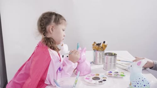 Little Girl Painting Paper Mache Figurines with Acrylic Paint for Her Homeschooling Art Project