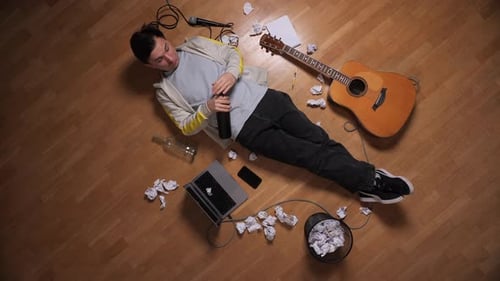 Man Lying on the Floor Surrounded By Crumpled Papers a Guitar and a Microphone Struggling with