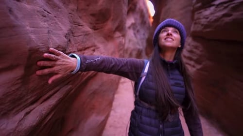 Schöne Wanderin reibt sich beim Gehen die Hand an der Sandsteinwand einer engen Schlitzschlucht entlang
