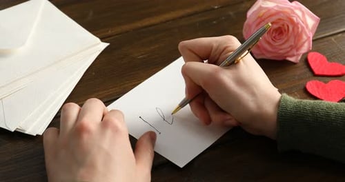 Woman writing phrase I Love You on card at wooden table, closeup