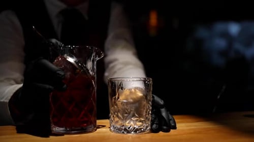 Bartender pouring drink from a glass bottle into glass with ice ready to serve final drink close-up