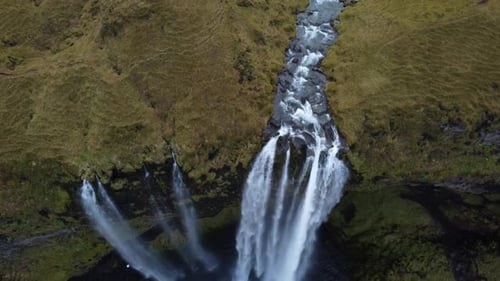 Winding River Flowing Down Series of Small Waterfalls on Green Hillside