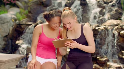 Cheerful young women using tablet computer and resting in sunny summer park
