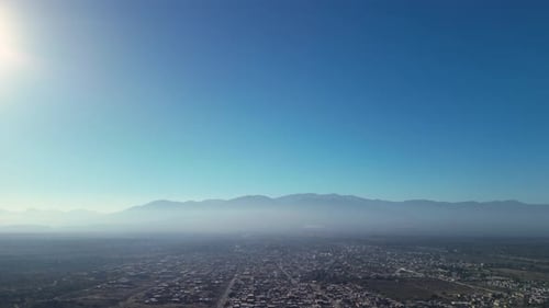 Aerial view drone flying over misty rural town with clear blue sky.