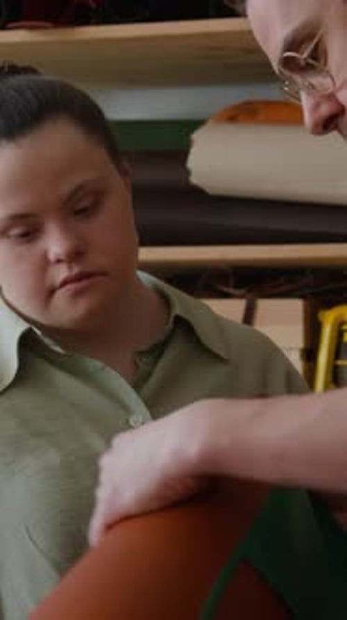 Person with Down Syndrome Examining Fabric Held by Craftsman in Leather Workshop