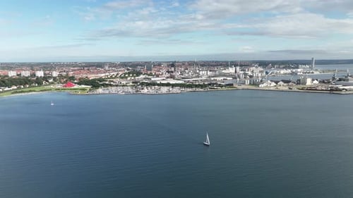 A sailboat cruising the bay of Aarhus Denmark - Summer aerial with panoramic cityscape background