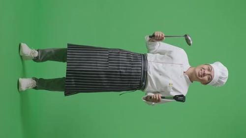 Full Body Of Asian Man Chef Smiling And Showing Tongs And Ladle To Camera In The Green Screen