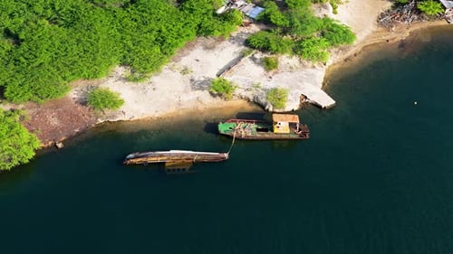 Drone orbit around rusted sunken or abandoned boat anchored off white coastal sandy beach