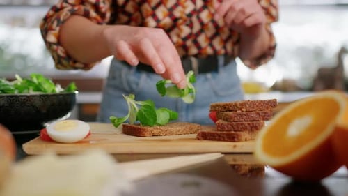 Close-up of girl putting cheese and vegetables on sandwich, no face