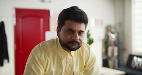 Portrait Of Indian Marketing Professional Leaning On Desk In Modern Well Lit Office During The Da...