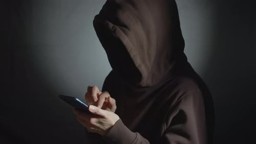 Hooded Figure Using a Smartphone in the Shadows
