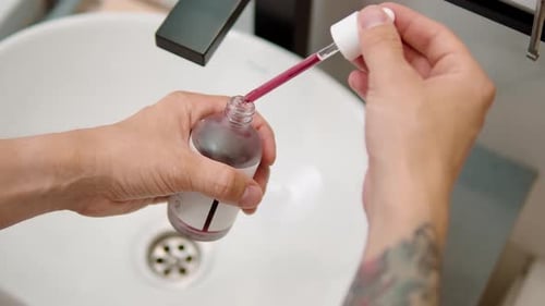 Man Holding Dropper with Red Cosmetic Serum Over Sink