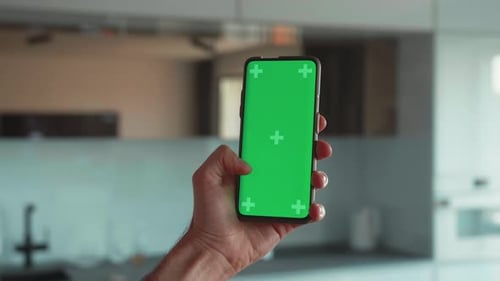 Handheld Camera Point of View of Man at Modern Room Sitting on a Chair Using Phone With Green Mockup