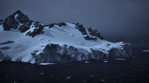 Forschungsschiff bewegt sich unter dunklem Himmel in Richtung schneebedeckter Küste