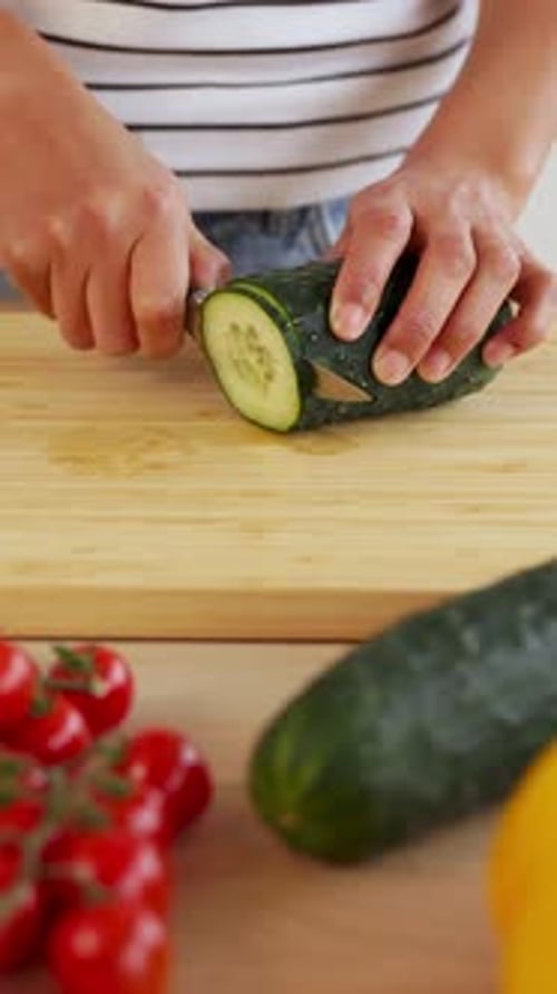 Close Up Woman Hands Slicing Fresh Cucumber on Wooden Cutting Board in Kitchen