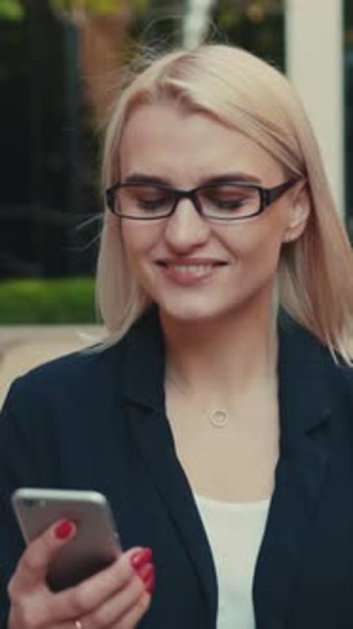 Smiling Beautiful Young Woman with Glasses Walks Down the Central City’s Street Uses Phone