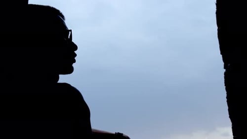Silhouette einer Person, die auf dem Hintergrund des blauen Himmels sitzt