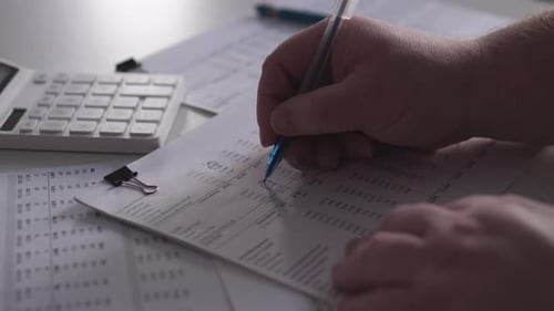 Weißer Mann prüft Jahresabschlüsse auf Zwischenablage mit Taschenrechner und Stift Methodische Überprüfung von