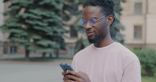 Cheerful African American Man Using Smartphone Texting Standing in City Street Busy with Online