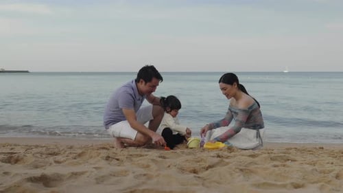 toddler baby girl playing sand toy with father and mother. happy family on the sea beach in Pattaya