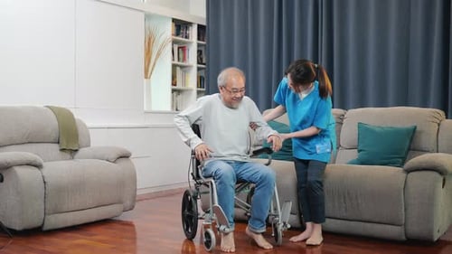 Caregiver Helping Senior Man Stand from Wheelchair