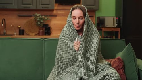 Une femme brune mécontente et bouleversée est assise à la maison sur un canapé vert, souffrant d'un rhume et utilisant