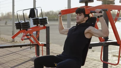 Muscular Man Engages in an Intense Street Workout Targeting His Shoulder Muscles As He Lifts Weights