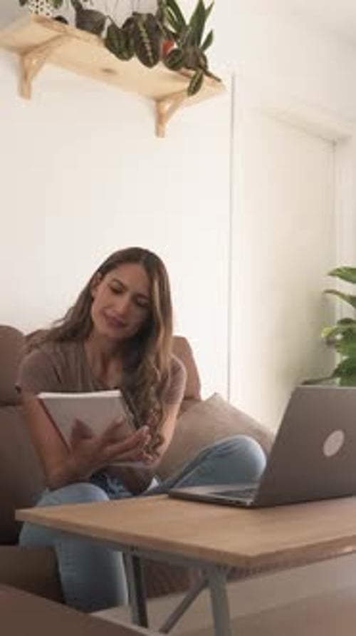 Woman works on laptop and takes notes at home