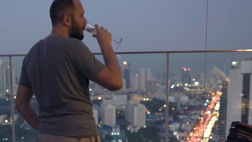 Young Man Drinking Cocktail and Admire View From Terrace in Bar At