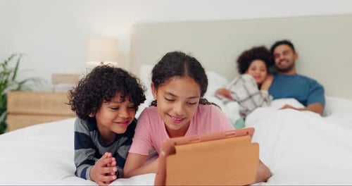 Children Using Tablet with Parents Lying in Background