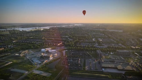 Colorful hot air balloon flying over buildings in small european city at summer sunset, aerial view,