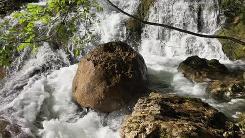 A Turbulent Stream of a Mountain Waterfall with a Large Round Stone in the Middle