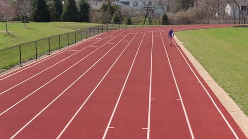 Teen girl on a track breaks into a run towards and past camera on a pretty day.