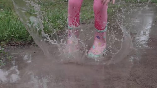 Young Caucasian girl laughing hard after she jumps up and down in puddle splashing water, handheld p