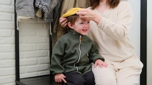 The parent puts a yellow scarf on their baby's neck before going out in the cold weather. A woman pu