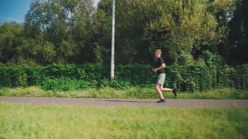 Running Cardio Workout Young Caucasian Man Runs in the Morning in the City Park with Lush Vegetation