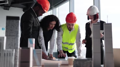 Gemischtrassige Mitarbeiter, Bauherren und Architekten stehen mit Bauplänen am Tisch