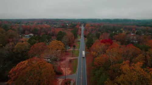 Aerial view of a truck driving along a rural road surrounded by vibrant autumn foliage in Fort Payne