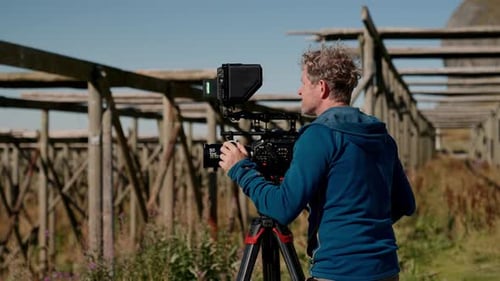 Filmmaker Adjusting Video Camera Outdoors on Tripod
